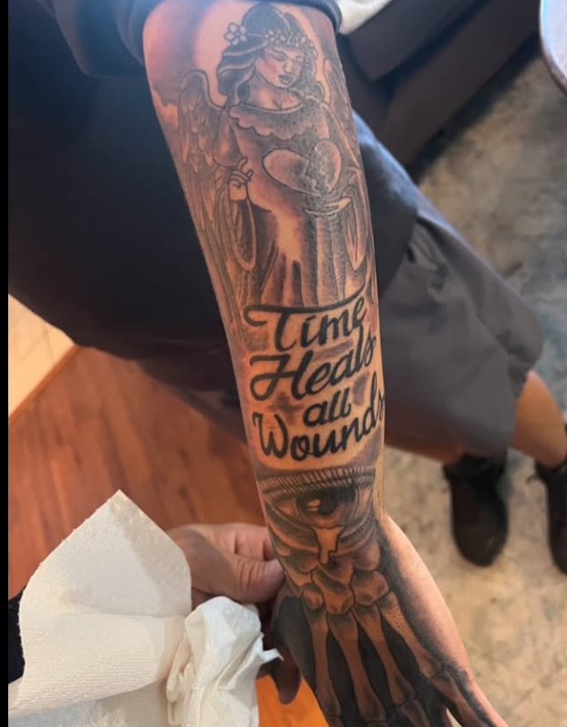 Forearm tattoo of an angel, text 'Time Heals all Wounds', and an eye with a tear