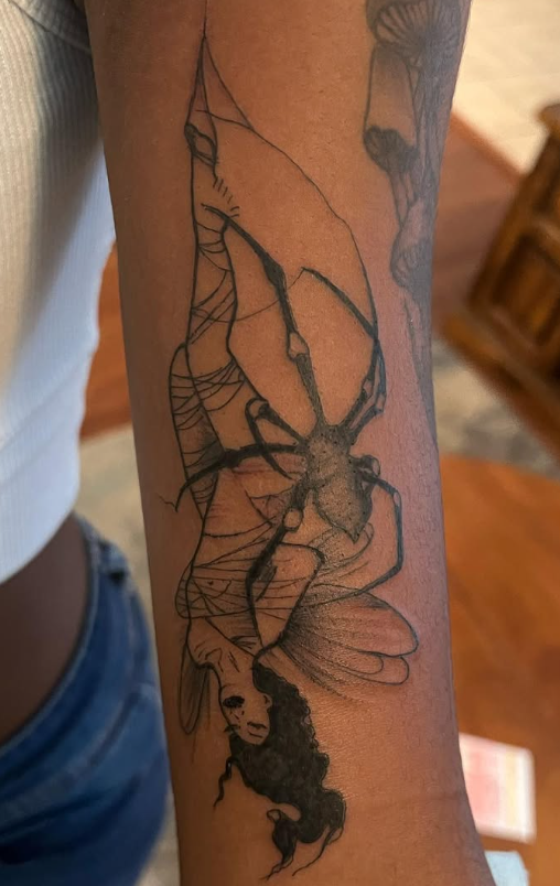 Forearm tattoo of a figure wrapped in webs with a spider and a face