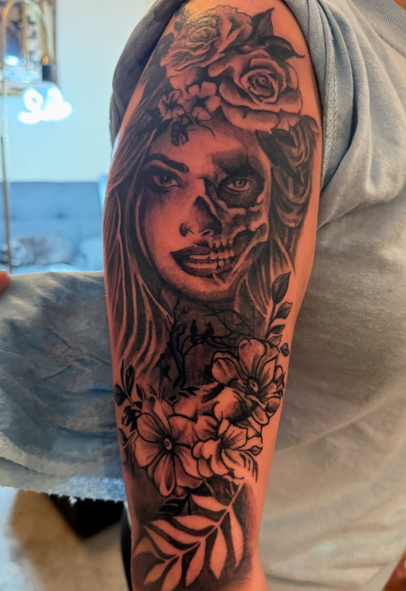 Arm tattoo of a woman's face transforming into a skull with flowers