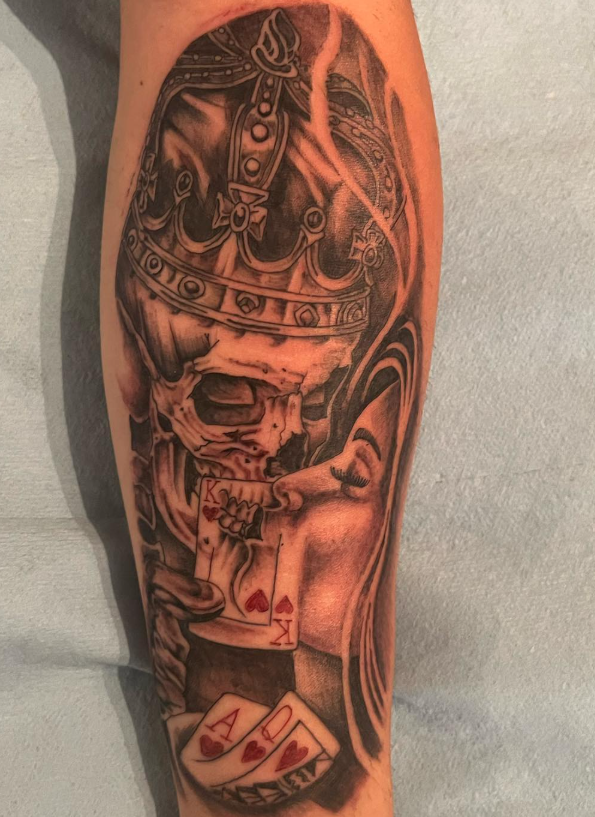 Leg tattoo of a skull with a crown, a woman's face, and playing cards