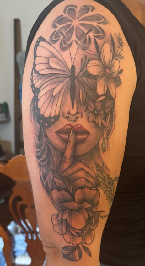 Arm tattoo of a woman's face with a butterfly and finger to lips