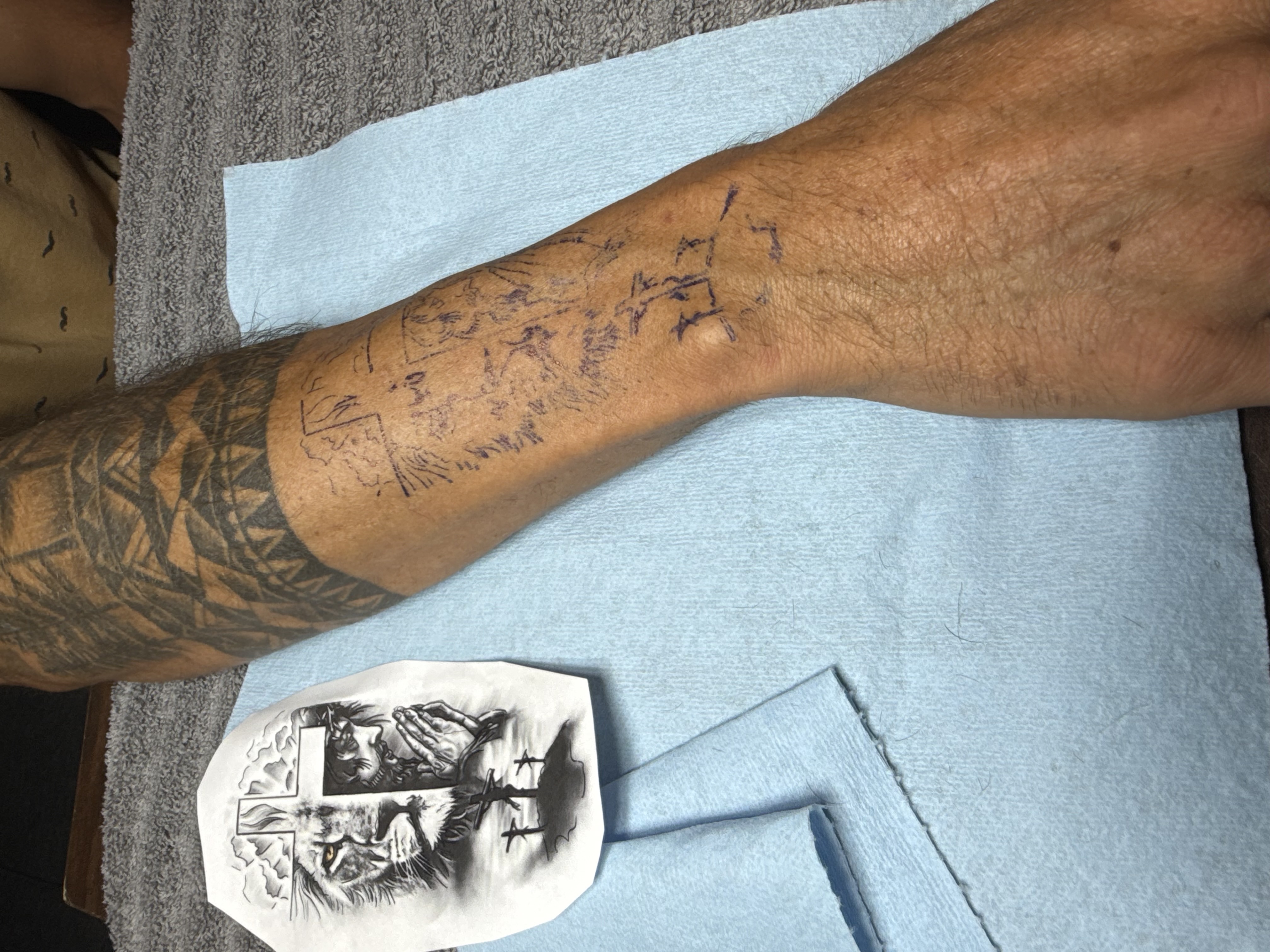 Religious leg tattoo in progress featuring a lion, Jesus figure, and crosses with stencil visible